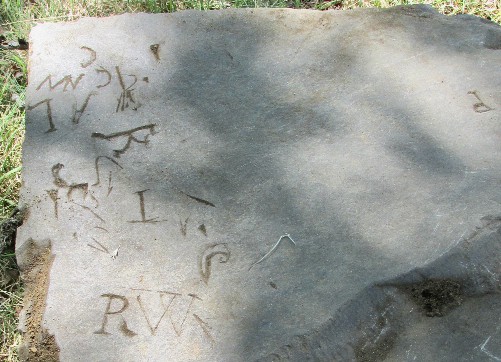 slate fragment showing random marks and letters scratched into the stone