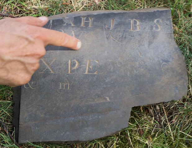 slate fragment, person's finger oints to the letters carved into it