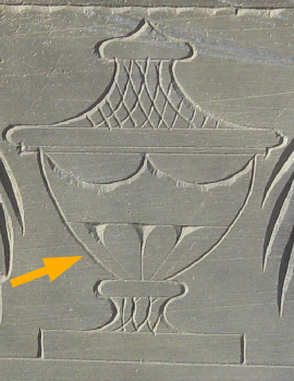 detail from an urn carved into a slate stone with a superimposed yellow arrow poiniting to the 3 flutes of the urn
