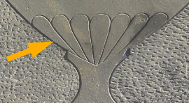 detail from the bottom of an urn carved into a slate stone with a superimposed yellow arrow pointing to the 7 flutes of the urn