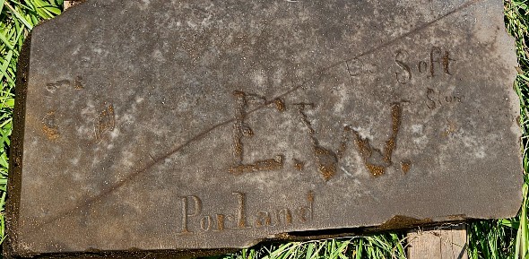 detail from the bottom of a slate gravestone carved with soft stone, E.W. and Portland