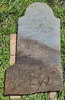 slate gravestone on the ground, supported with 2 lumber pieces, E.W. is prominently below the burial line