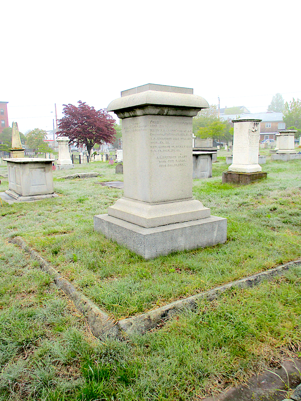 a marble monument set in a cemetery with green grass and a granite border around the plot